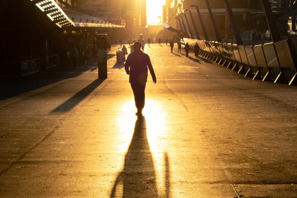 silhouetted figure walking on a city street in the bright light of sunset.