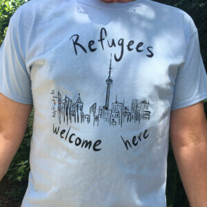 photo of a blue t-shirt that shows a drawing of the Toronto skyline surrounded by the words "Refugees welcome here"