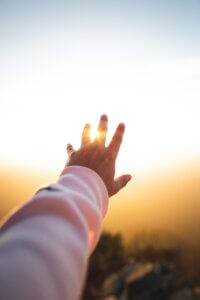 a hand reaches toward the sunset