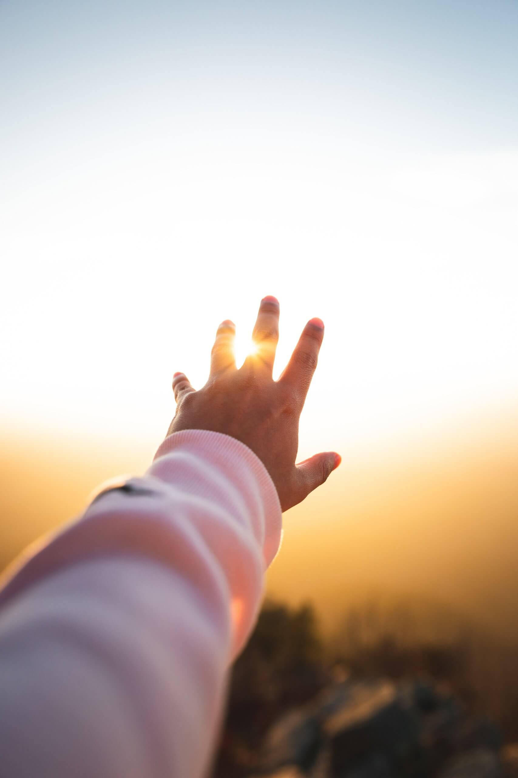 a hand reaches toward the sunset