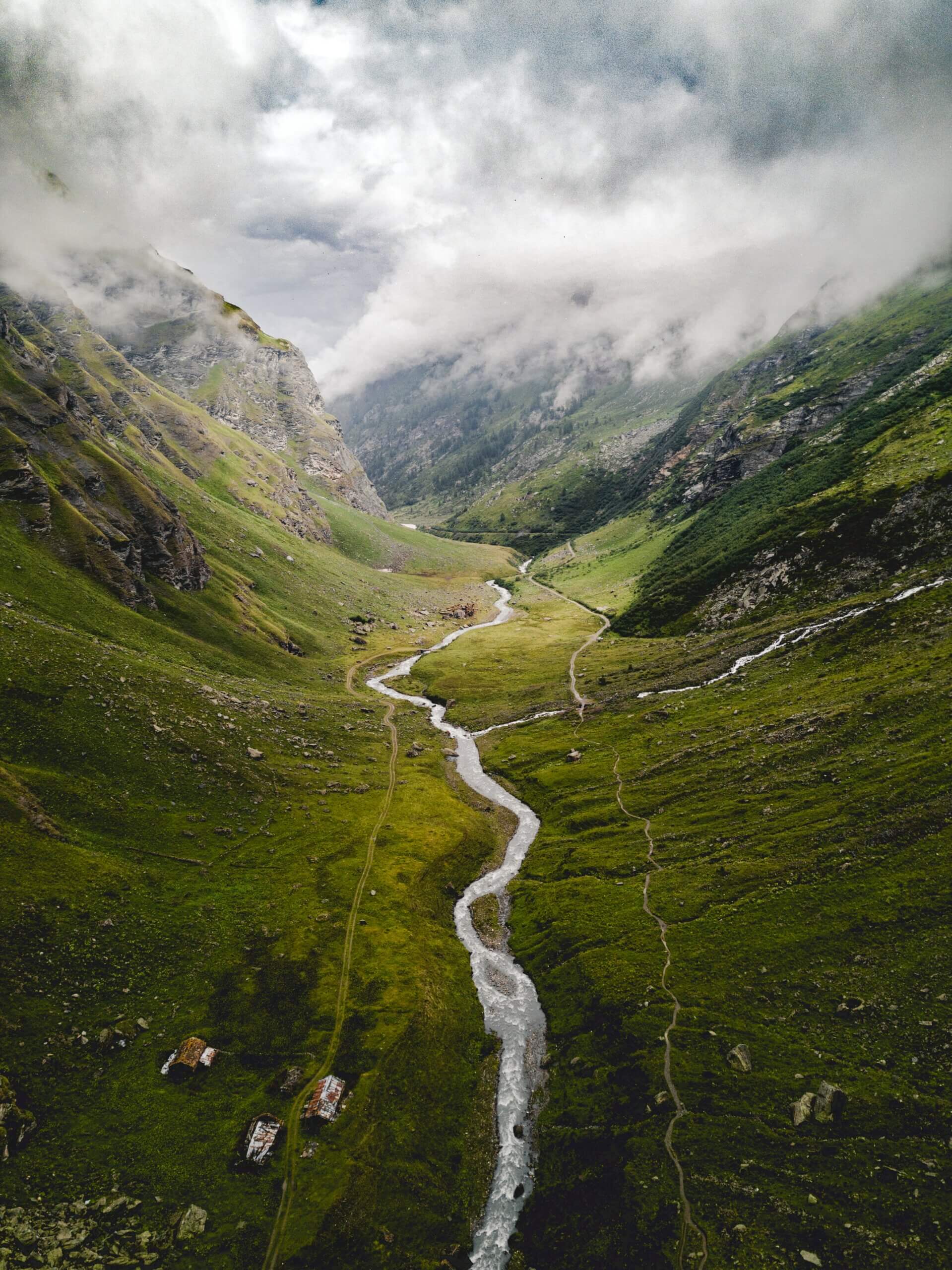 a river cuts between two lush mountains on a cloudy tumultuous day