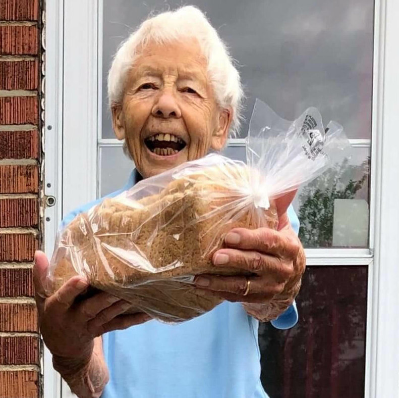 A smiling older woman holds out a loaf of sandwiches she has made to share with the hungry