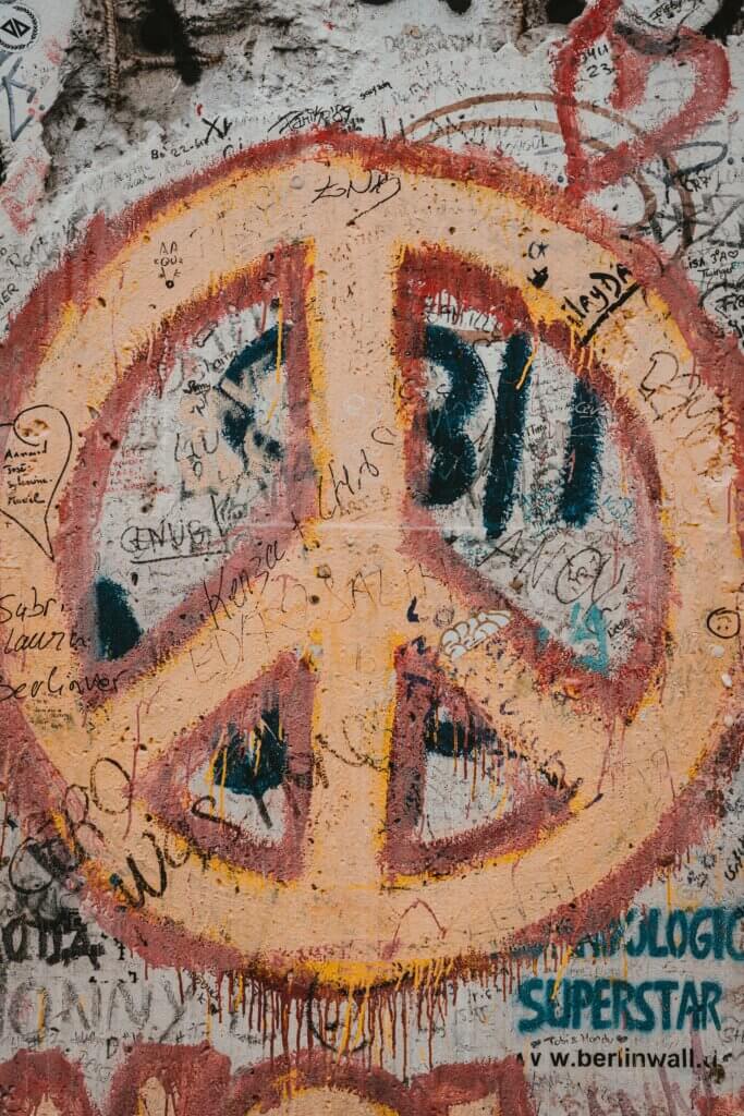 An orange peace sign painted in graffiti over a mish-mash of other graffiti.
