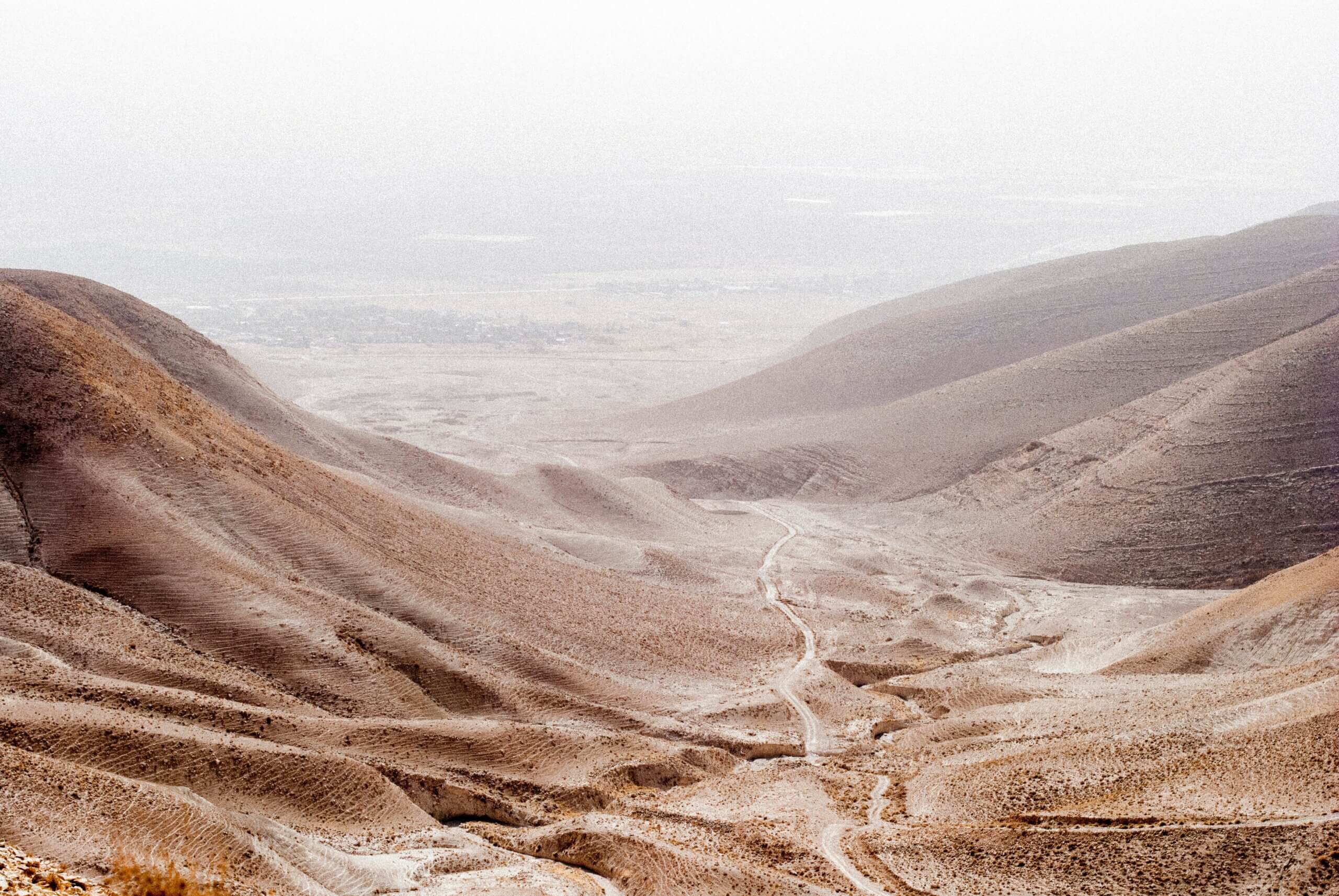 a path travels down through a gap between low mountains into a misty desert valley.