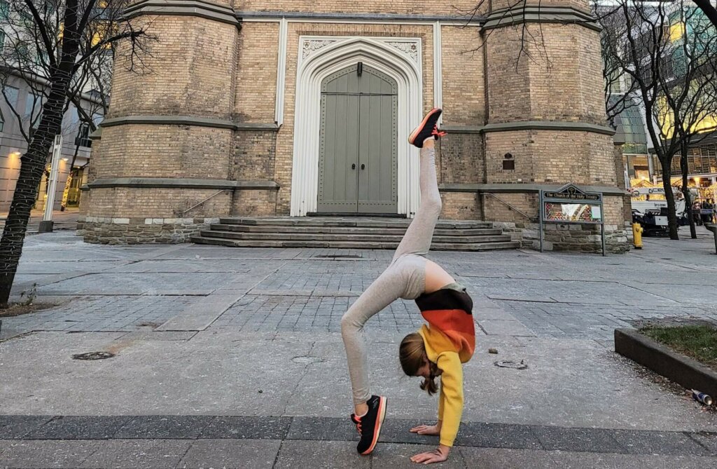 A young person does a backbend and handstand outside the west doors of Holy Trinity