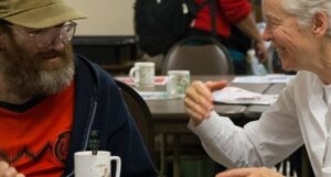 An older woman talks with a middle-aged bearded man over coffee