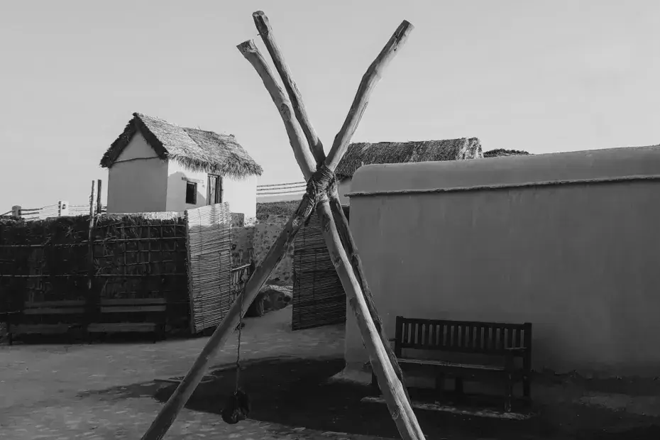 a wooden tripod stands outside a number of huts